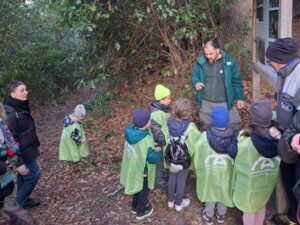 Un naturalista spiega a un gruppo di bambini l'importanza di piantare alberi davanti al cartello di un parco